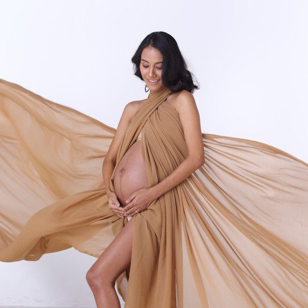 Portrait of Pregnant Asian Indian tanned skin woman brown gold fabric fluttering in Air, Lady with throwing textile waving fashion style, Studio lighting white background